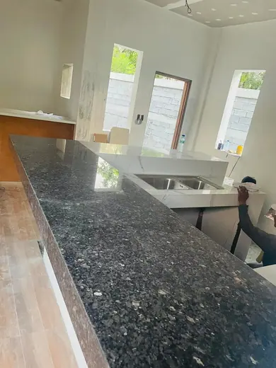 Long dark speckled kitchen island beside a sink during installation