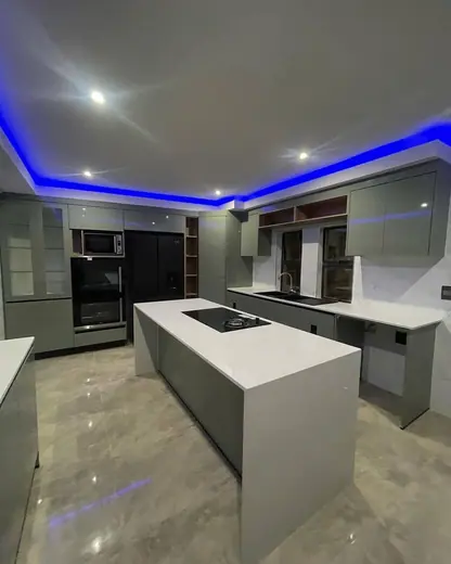 Modern kitchen with a long white island beneath blue ceiling lighting